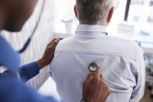 A doctor is using a stethoscope to listen to a man's lungs