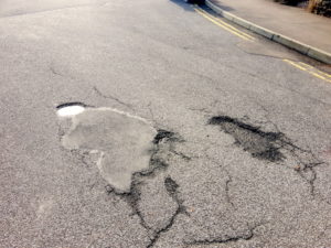 Damaged road surface showing a hole and also an area where it has been mended before