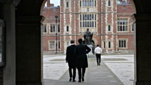 Back view of schoolboys at Eton walking through a very smart courtyward. The boys are wearing long black formal jackets