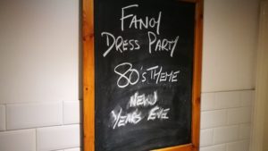 Chalkboard on pub wall with the words 'Fancy dress party 80's theme new years eve'