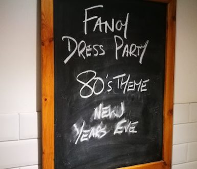 Chalkboard on pub wall with the words 'Fancy dress party 80's theme new years eve'