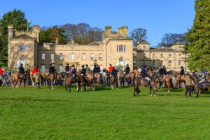 Group of people on horses in front of a large country house. The people are wearing clothes used for foxhunting