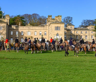 Group of people on horses in front of a large country house. The people are wearing clothes used for foxhunting