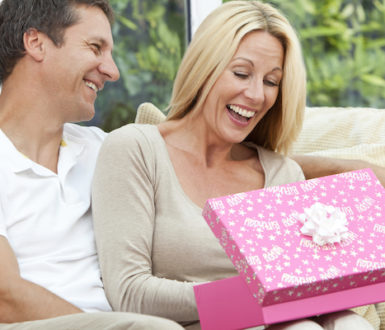 Woman looking fairly excited about a gift she has just opened. A man sits next to her