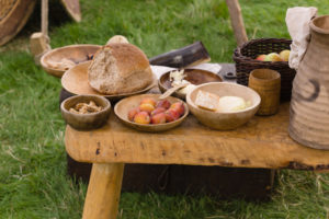 Food from medieval times arranged on wooden plates. Bread, walnuts, plums, apples. Also mead in a ceramic jug.