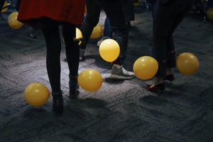 the legs of people dancing, with yellow balloons floating about