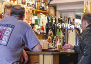 Men sitting at the bar of a pub in front of different beer and ale pump handles