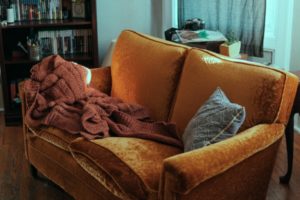 Sofa in a living room. On the sofa is a blanket and cushion