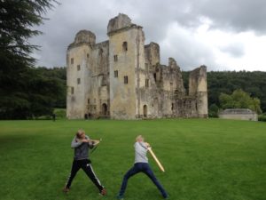 Boys fighting with wooden weapons outside ruined castle 