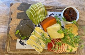 British cheeses on a board with sliced apple and pear and a pot of chutney