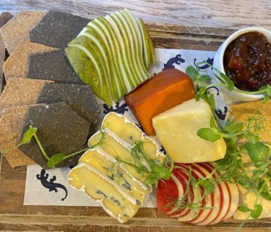 British cheeses on a board with sliced apple and pear and a pot of chutney